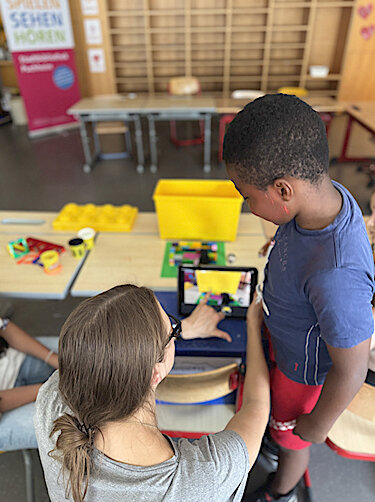 Workshopleiterin und ein Kind arbeiten an einem iPad